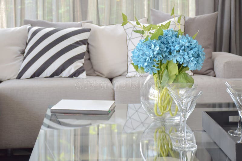 Light blue flower and wine glasses on center table with striped black and white pillow and gray tone pillows on beige sofa royalty free stock image