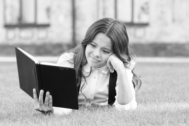 Literature for kids. Lesson on fresh air. Cute small child reading book outdoors. Schoolgirl school uniform laying on. Lawn with favorite book. Studying concept royalty free stock photography