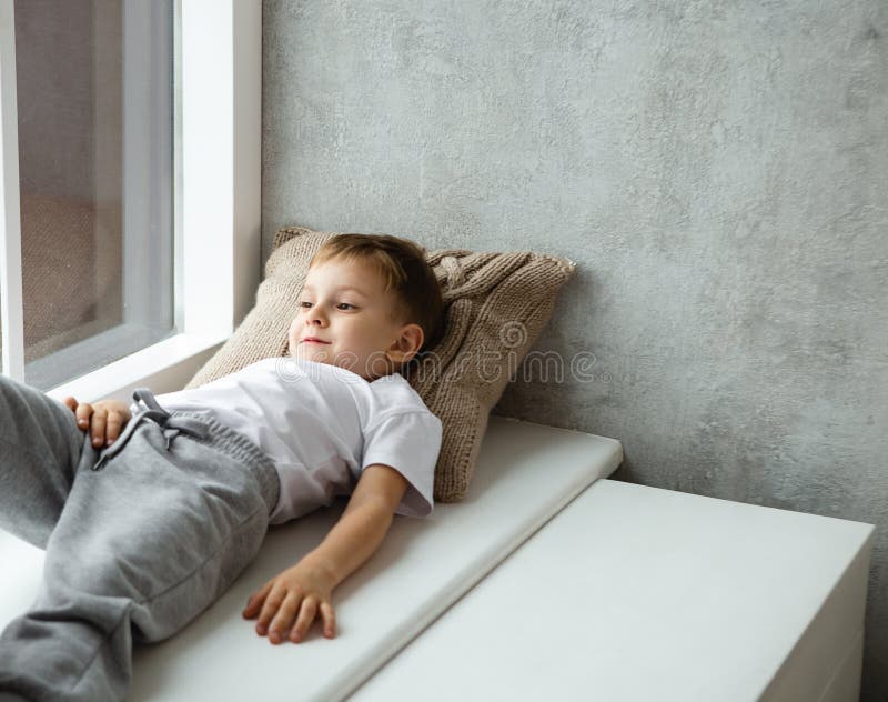 Little child boy lies on knitted pillow on windowsill indoor. Knitted style in the interior. Warm and cozy. Playful children royalty free stock images
