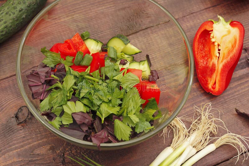 Making summer salad of fresh summer vegetables and herbs in glass bowl on rustic wooden table. Making summer salad of fresh summer vegetables and herbs in a royalty free stock photography