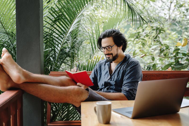A man reads notes in a diary at a table with a laptop and morning coffee on the terrace of a country house. A man reads notes in a diary at a table with a laptop royalty free stock photo
