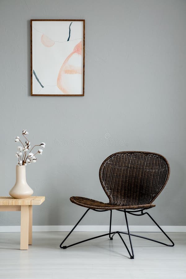 Modern armchair next to wooden table with flowers in grey interior with poster on the wall. Real photo royalty free stock image