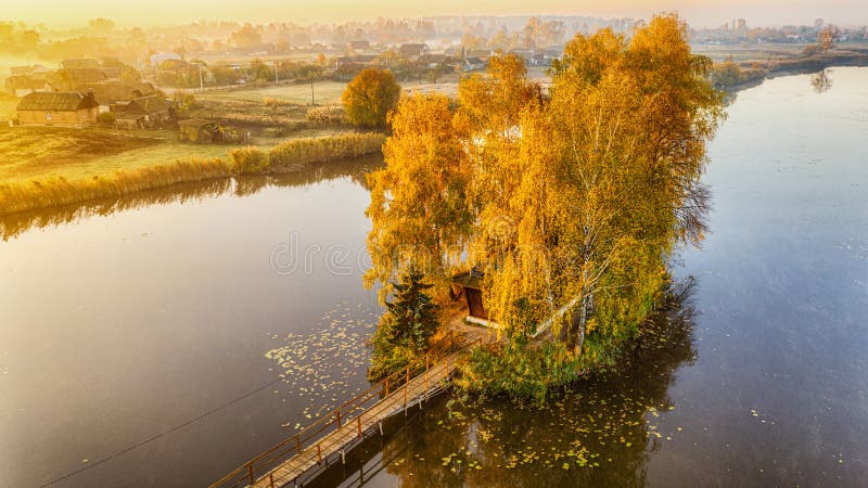 Morning landscape, wooden hunting lodge, on a small man-made island. A wooden platform is coming to the house, birch trees are stock image