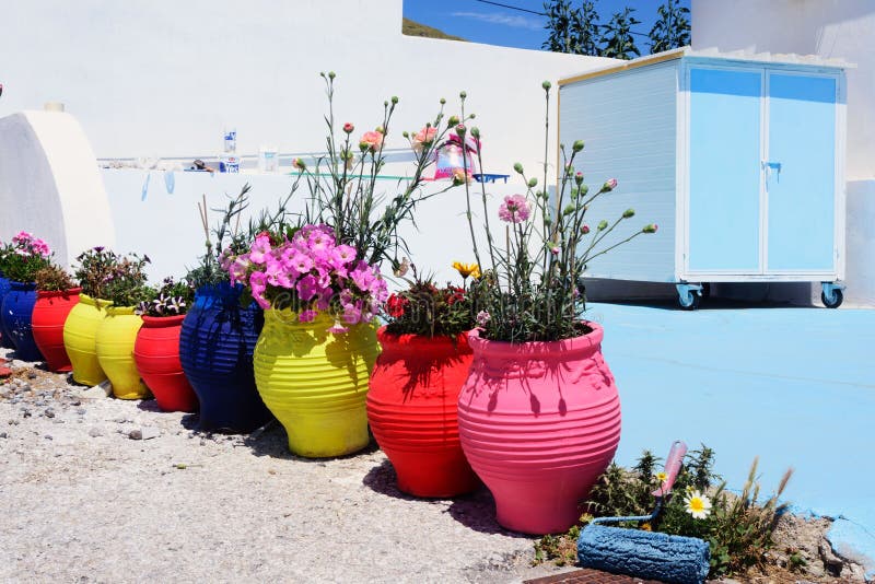 Multi-colored clay pots with flowers under the bright sun. Renovation in a traditional greek house with white and blue paint. stock photo