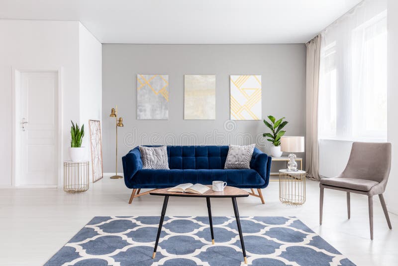 Open space living room interior with modern furniture of a navy blue settee, a beige armchair, a coffee table and other objects in stock photo