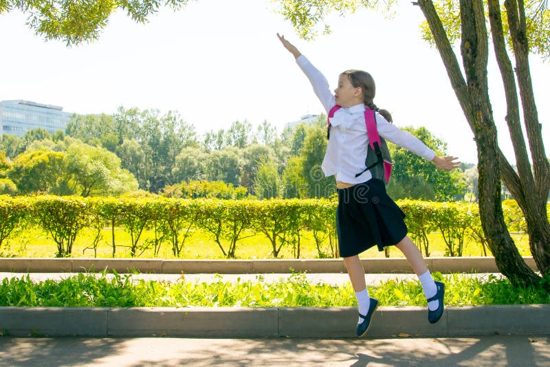 In the park, in the fresh air, a schoolgirl is having fun and jumping up, raising her hand stock photo