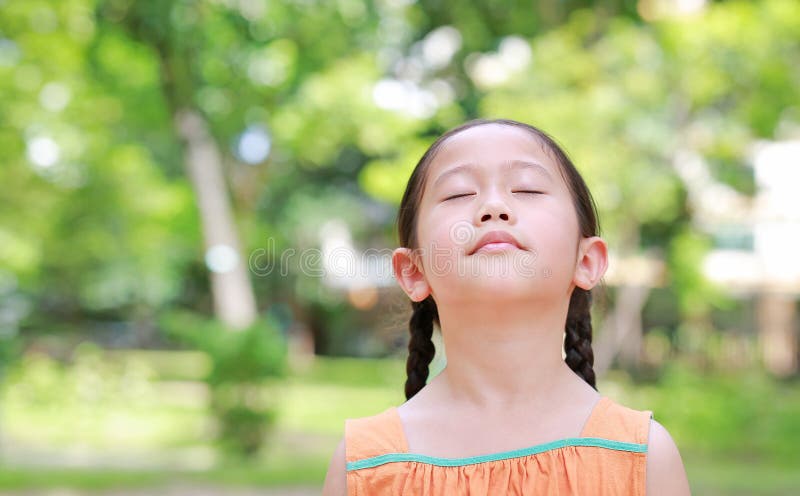 Peaceful little Asian child girl close their eyes in garden with Breathe fresh air from nature. Portrait of kid relax in green. Park for good health royalty free stock image