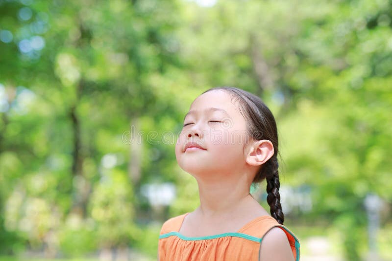 Portrait of happy Asian child close their eyes in garden with Breathe fresh air from nature. Close up kid girl relax in green park. For good health royalty free stock photography