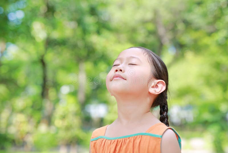 Portrait of happy Asian child close their eyes in garden with Breathe fresh air from nature. Close up kid girl relax in green park. For good health stock images