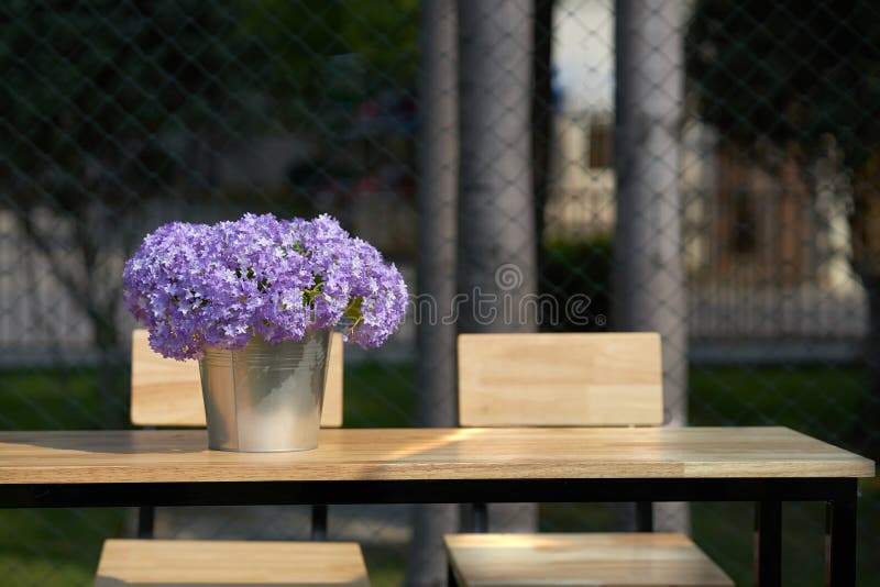 Purple flowers in bucket vase on wooden table with chairs with s. Unlight and shade royalty free stock photography