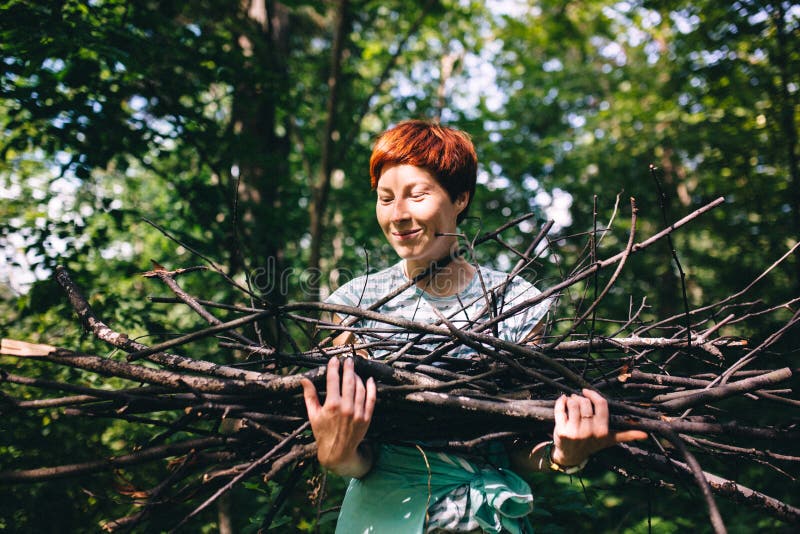 Red-haired hipster girl collects firewood on the background of the forest. Processing under the film stock photos