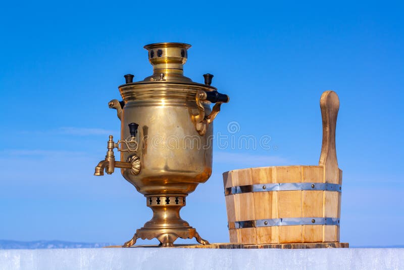 Retro copper samovar and a wooden tub for water stand on an ice plate against a blue sky. royalty free stock image