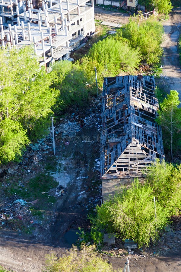 Ruined wooden house on the background of the erection of a new building - renovation program. Demolition of low-rise buildings royalty free stock image