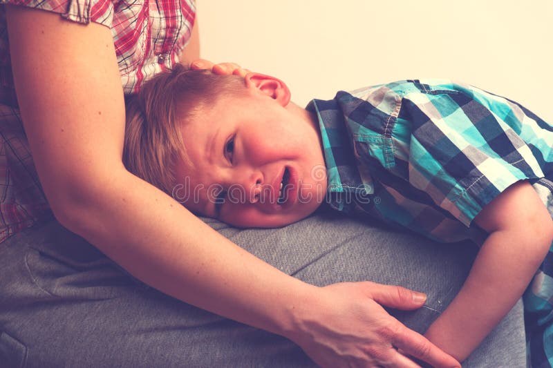 Sad little crying boy hugging his mother at home. Woman comforting her unhappy child. Family relations problems stock photo