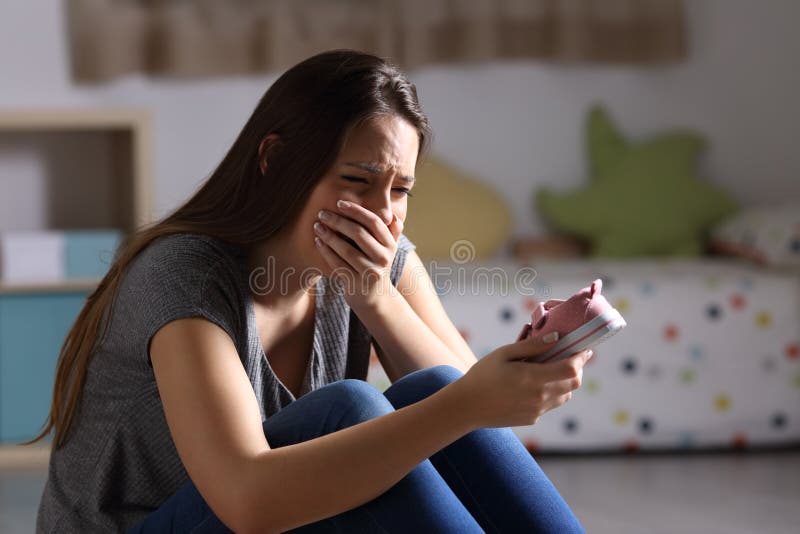 Sad mother missing her daughter. Holding a little shoe sitting on the floor of the bedroom in a house interior with a dark background royalty free stock images