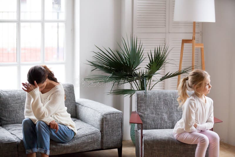 Sad tired mother and sulky daughter not talking after conflict. Sad tired mother and sulky angry offended child girl not talking after conflict in living room royalty free stock photography