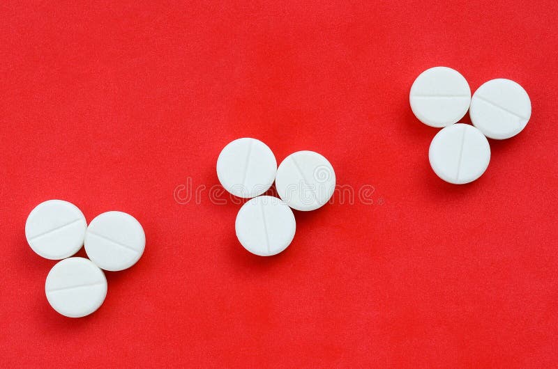 Several white tablets lie on a bright red background in the form of three triangular arrows. Background image on medicine and phar royalty free stock photos