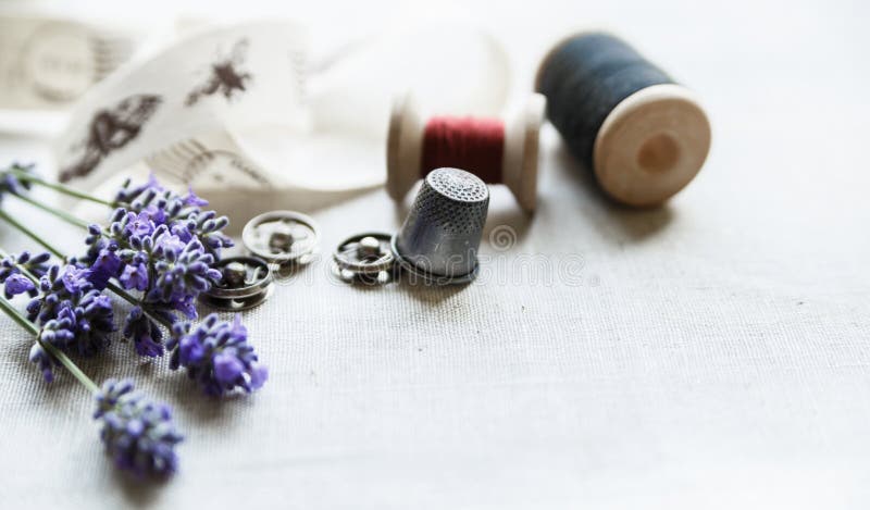 Sewing tools with fresh lavander flowers on linen background. Vintage wooden spool, braid, thimble, buttons. stock image