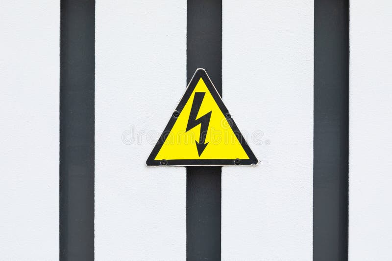 Small yellow triangular sign with black lightning on black and white striped wall stock photo