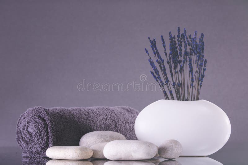 Spa. Lavender flowers stand in a white vase on a gray background. Pebbles and a towel rolled into a roll royalty free stock photo