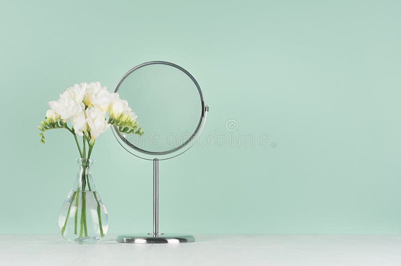 Spring fresh white flowers with elegant round mirror on white table and green mint menthe wall, interior. royalty free stock photography