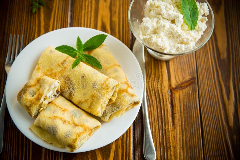 Sweet fried thin pancakes with cottage cheese inside. On a wooden table stock image