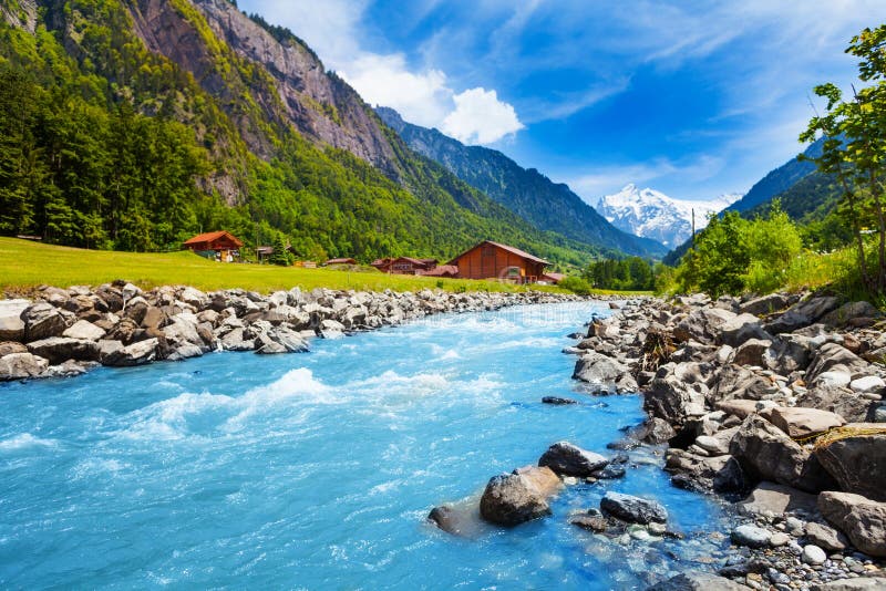 Swiss landscape with river stream and houses. Breathtaking Swiss landscape with river stream, rocks and houses with Alps background in a sunny summer day royalty free stock photo