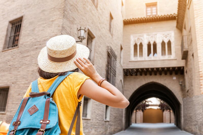 Woman in hat with backpack looking at the Gothic balcony and arch hidden place in old town of Zaragoza, Spain. Tourist Woman in hat with backpack looking at the royalty free stock images