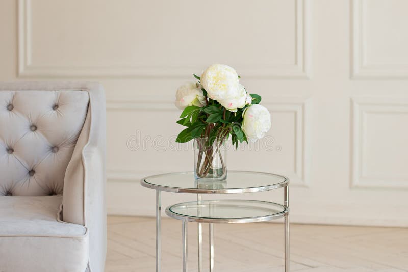 Vase with beautiful peony flowers on table near a grey sofa in living room. Cozy home decoration, fresh white peonies on coffee ta royalty free stock photo