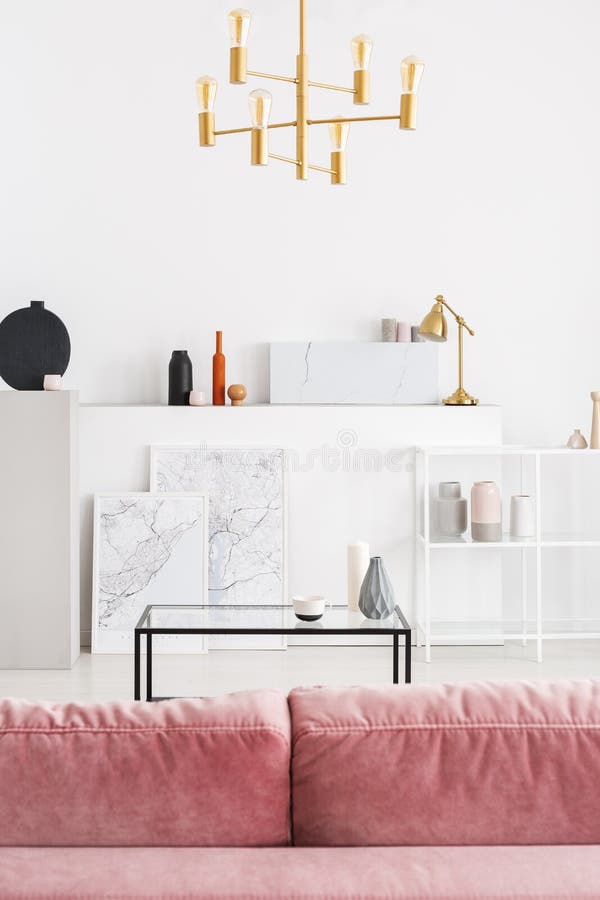 Vertical view of backside of powder pink sofa in white modern living room interior with coffee table, golden chandelier and maps. In white frames, real photo royalty free stock image