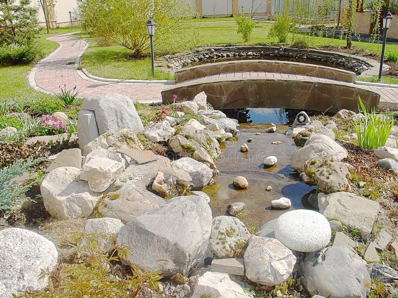 View of landscape design called Alpine slide. Decorative watterfall , colorful rocks and green plants. Little bridge. View of landscape design called Alpine royalty free stock photos View of landscape design called Alpine slide. Decorative watterfall , colorful rocks and green plants. Little bridge. View of landscape design called Alpine royalty free stock photos