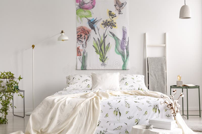 Wall art of flowers and birds painted on a fabric above a bed which is dressed in green plants pattern on white bedding in a fresh royalty free stock photography