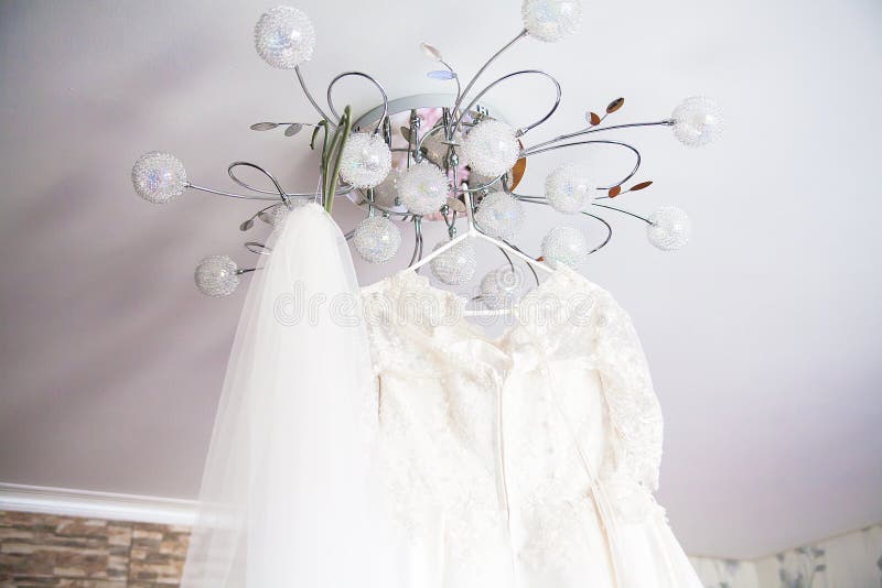Wedding dress embroidered with beads hanging on chandelier. White wedding dress embroidered with beads hanging on chandelier stock photo