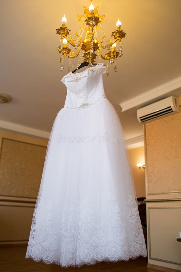 Wedding dress hanging on the chandelier. bride accessories. charges of the bride. bride`s morning.  stock image