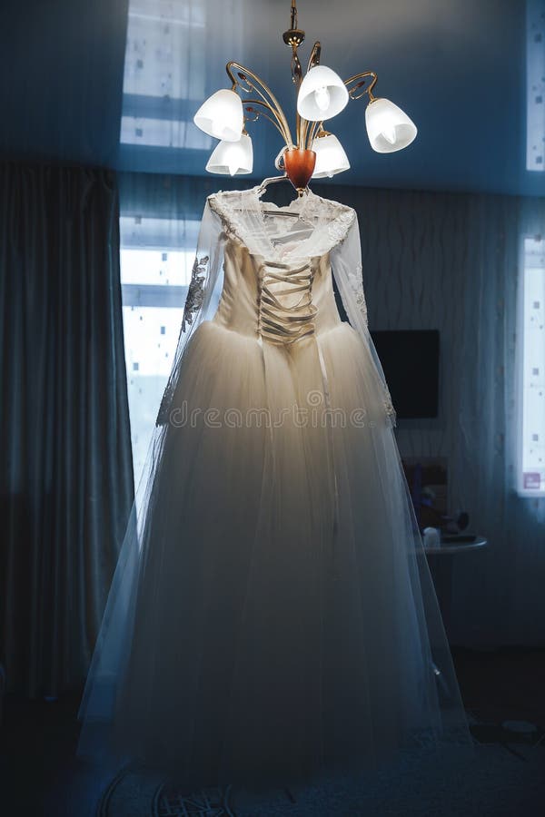 Wedding dress hanging on the chandelier. White wedding dress hanging on a glowing chandelier royalty free stock image