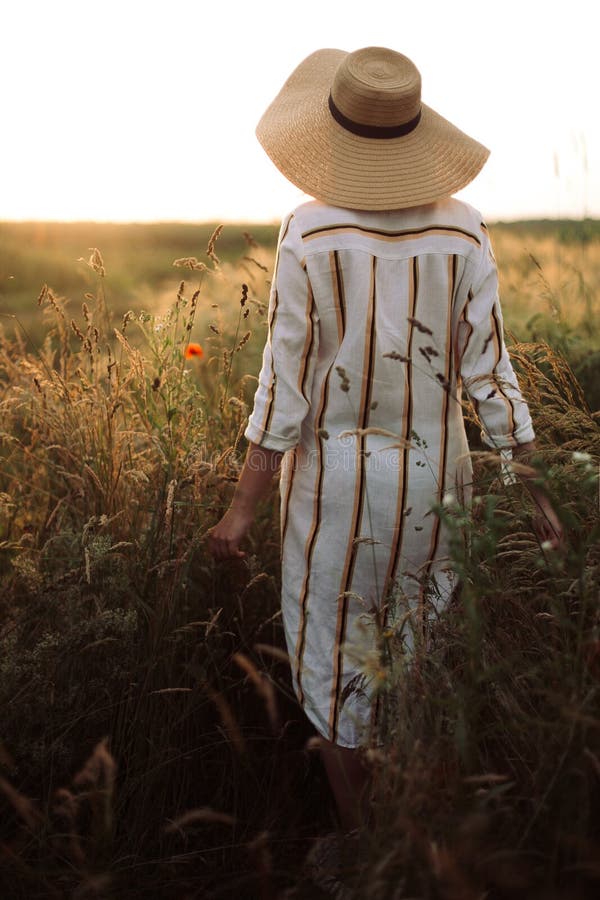 Woman in rustic dress and hat walking in wildflowers and herbs in sunset golden light in summer meadow. Atmospheric authentic. Moment. Stylish girl enjoying stock photos