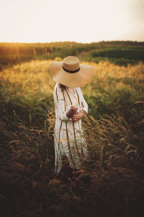 Woman in rustic dress and hat walking in wildflowers and herbs in sunset golden light in summer meadow. Atmospheric authentic. Moment. Stylish girl enjoying stock images