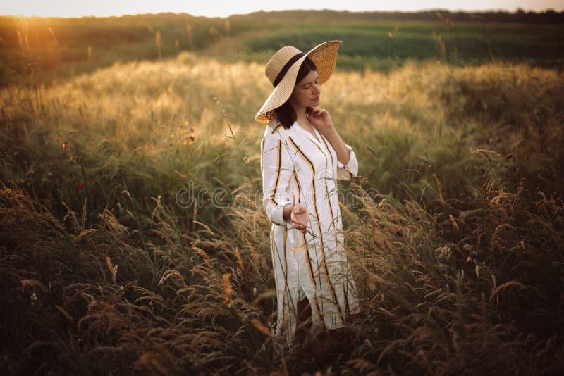 Woman in rustic dress and hat walking in wildflowers and herbs in sunset golden light in summer meadow. Stylish girl enjoying. Evening in countryside. Rural royalty free stock photos