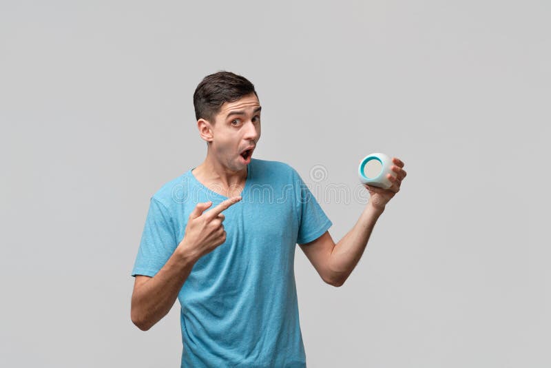 Young brunet man is shocked holding alarm-clock isolated over grey background royalty free stock photo