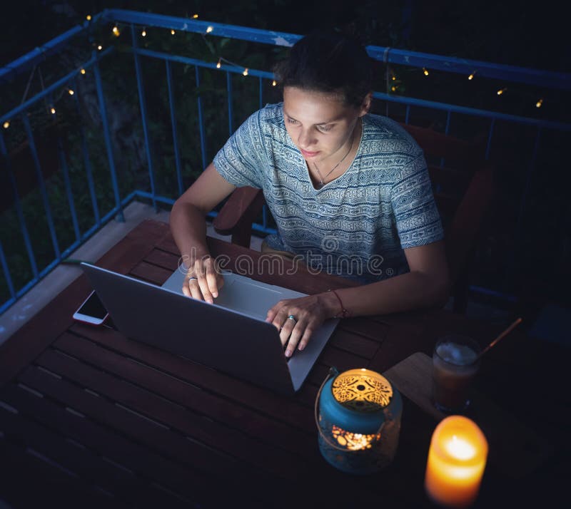 Young hysster woman working on a laptop in the evening on the open terrace of her country house, cozy with candles and lanterns.  stock photos