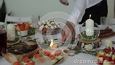 A young man in a white shirt lights candles which stand on the festive table among a variety of dishes with snacks and a stock video