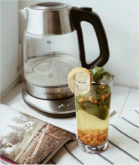 Чайник Polaris и облепиховый чай с лимоном и мятой в стакане стоят на подоконнике